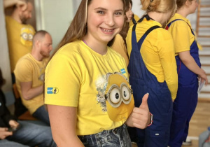 Uśmiechnięta uczennica w przebraniu minionka pokazuje znak OK